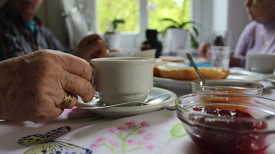 Die Hand einer alten Person greift nach einer Kaffeetasse an einem deckten Frühstückstisch