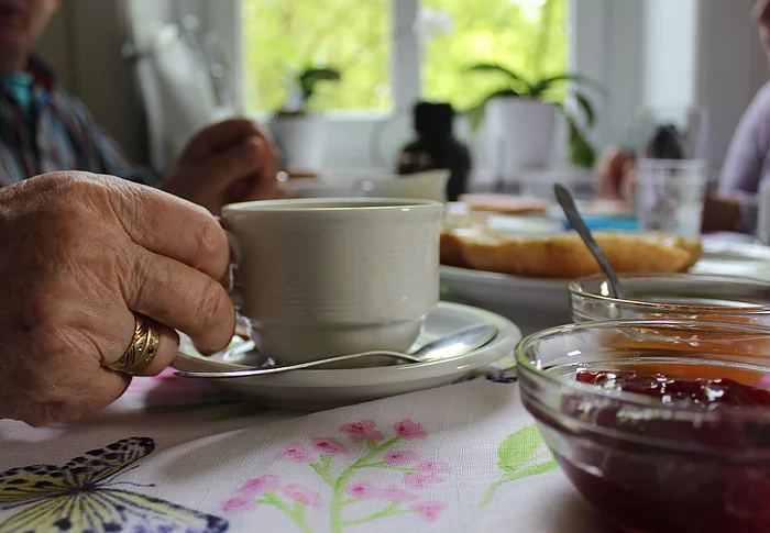 Die Hand einer alten Person greift nach einer Kaffeetasse an einem deckten Frühstückstisch