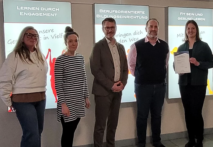 Fünf Personen stehen nebeneinander mit einer Urkunde in der Hand.