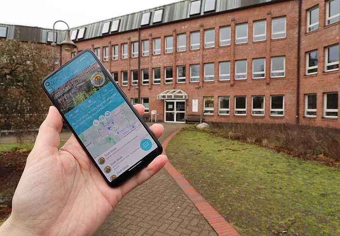 Eine Hand hält ein Smartphone mit der PPush-App vor dem Glinder Rathaus 