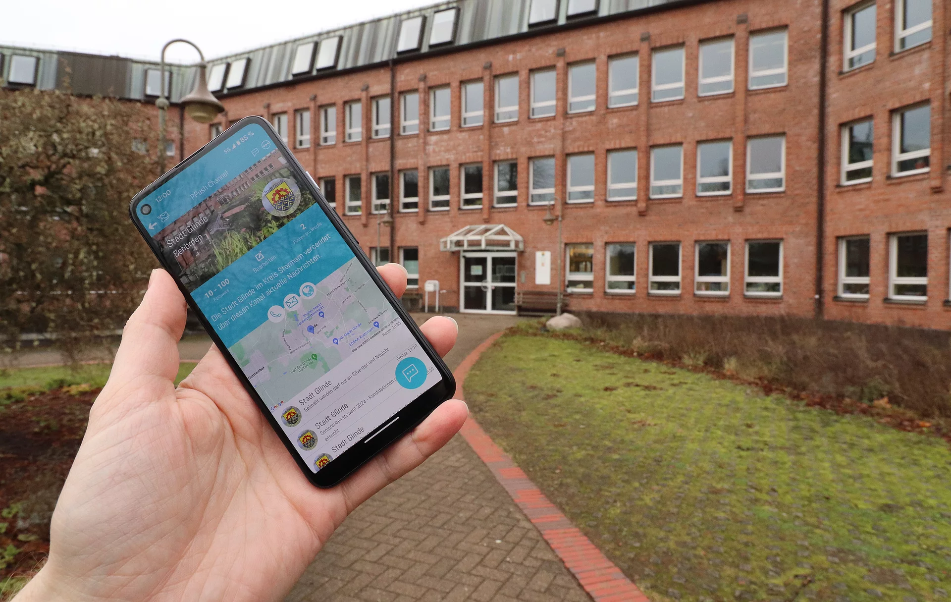 Eine Hand hält ein Smartphone mit der PPush-App vor dem Glinder Rathaus 