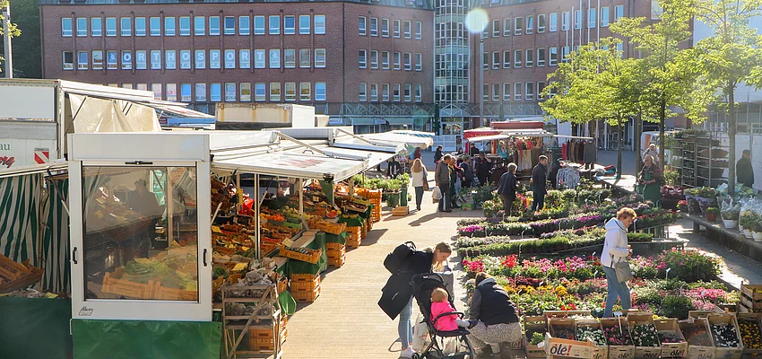 Menschen auf dem Wochenmarkt am Blumenstand und Obststand.