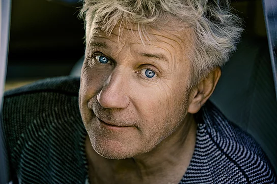 Der Schauspieler Jörg Schüttauf mit wuscheligen grauen Haaren und blauen Augen