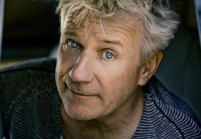 Der Schauspieler Jörg Schüttauf mit wuscheligen grauen Haaren und blauen Augen