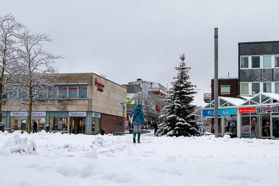 Der verschneite Markt. Eine Person geht durch den Schnee Richtung Weihnachtsbaum.