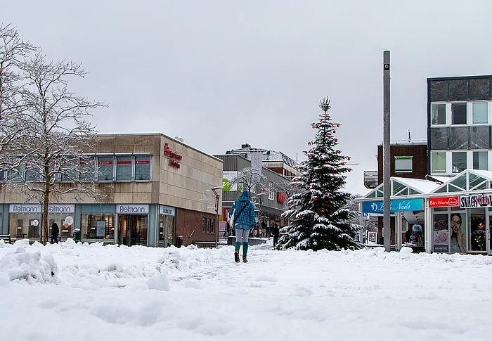 Der verschneite Markt. Eine Person geht durch den Schnee Richtung Weihnachtsbaum.