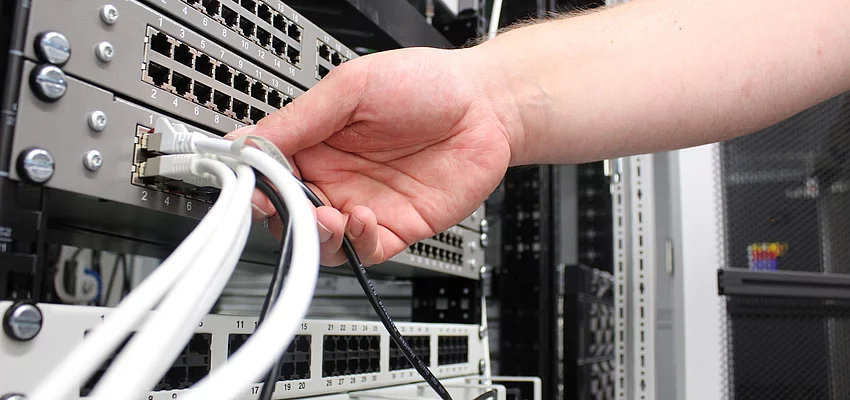Eine Hand greift nach einem Kabel an einem Server.