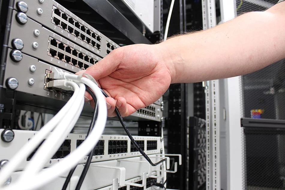 Eine Hand greift nach einem Kabel an einem Server.