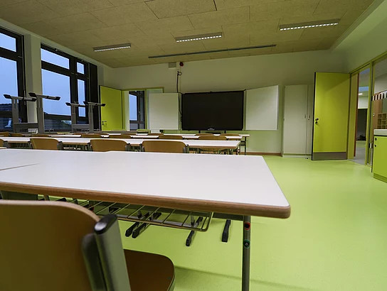 Ein in frischem Grün gehaltener Klassenraum mit einer digitalen Tafel im Hintergrund.