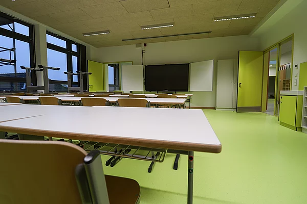 Ein in frischem Grün gehaltener Klassenraum mit einer digitalen Tafel im Hintergrund.