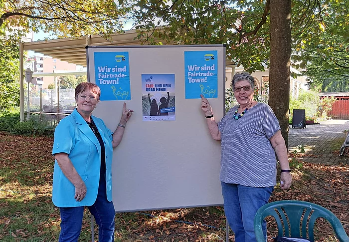 Zwei Frauen stehen vor einer Pinnwand mit Plakaten zum Thema Fairtrade