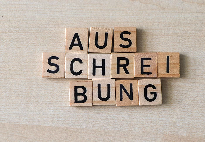 Holzplättchen formen das Wort Ausschreibung