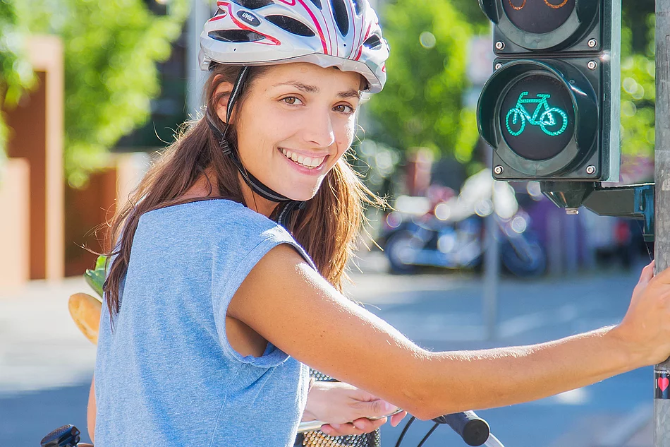 Eine Fahrradfahrerin mit Helm hält sich an einer Ampel fest.
