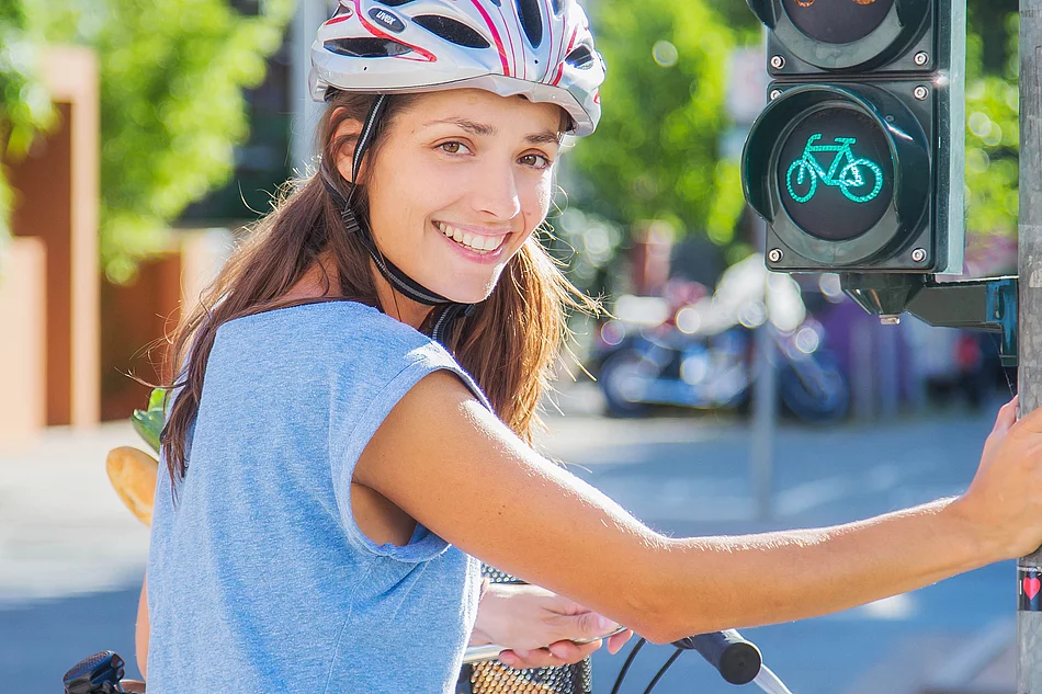 Eine Fahrradfahrerin mit Helm hält sich an einer Ampel fest.