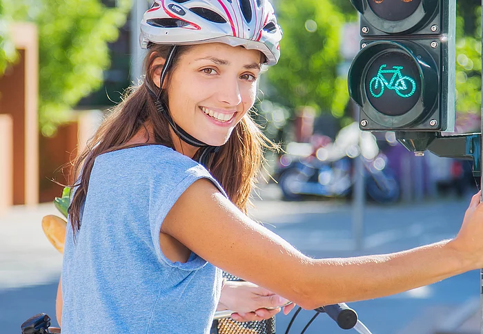 Eine Fahrradfahrerin mit Helm hält sich an einer Ampel fest.