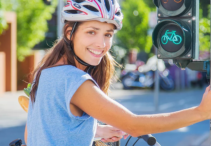 Eine Fahrradfahrerin mit Helm hält sich an einer Ampel fest.
