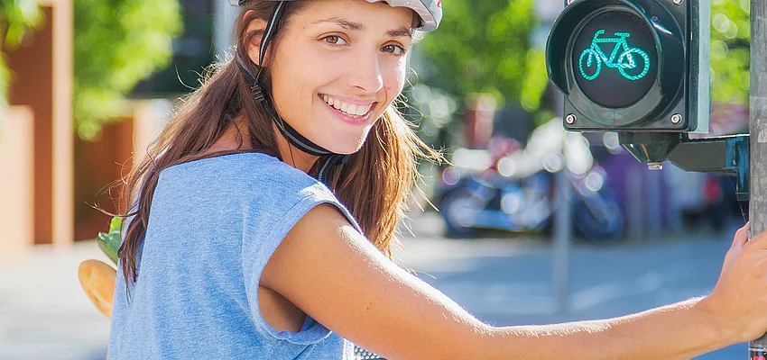 Eine Fahrradfahrerin mit Helm hält sich an einer Ampel fest.