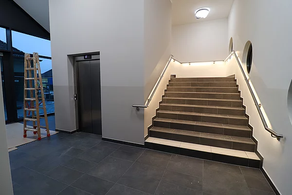 Blick in das Treppenhaus mit beleuchteten Handläufen und einem Aufzug.