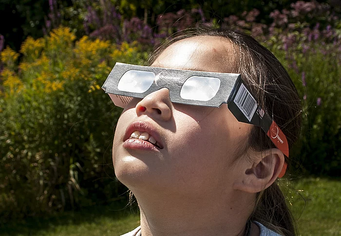 Ein Mädchen mit einer Schutzbrille schaut zur Sonne.