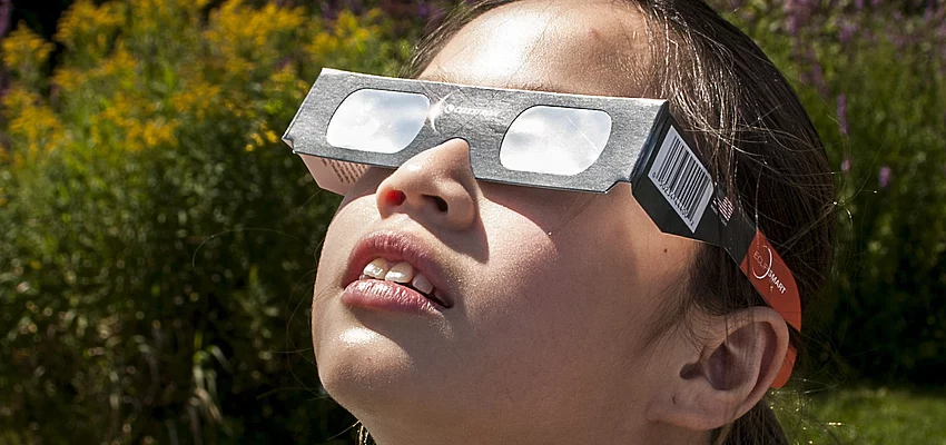Ein Mädchen mit einer Schutzbrille schaut zur Sonne.