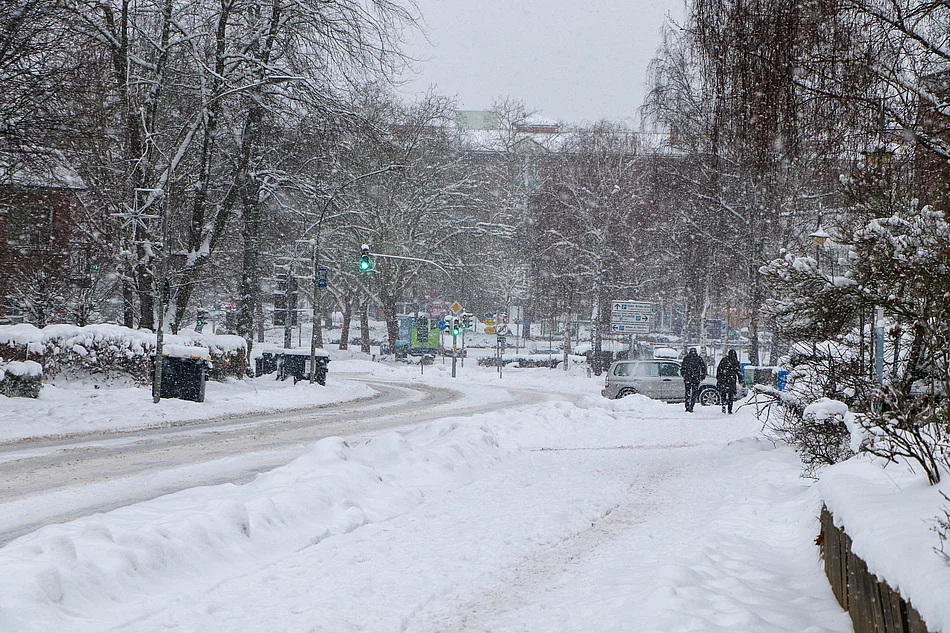 Es schneit, Menschen gehen den Oher Weg entlang und ein Auto biegt in eine Auffahrt ab.