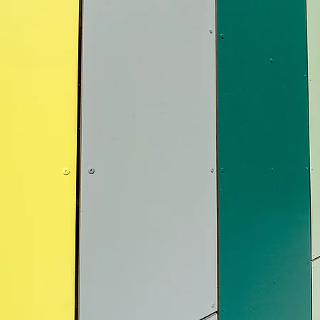 Die Fassade der Mensa Grundschule Tannenweg hat grüne, grau und gelbe Fassadeelemente.