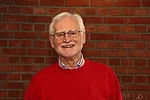 Ein Mann mit weißen Haaren, Brille und rotem Pullover.