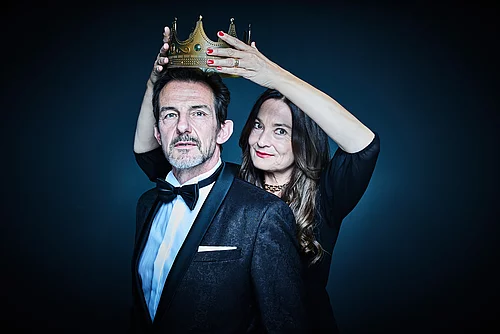Einem Mann in Anzug wird von einer Frau eine Krone aufgesetzt.