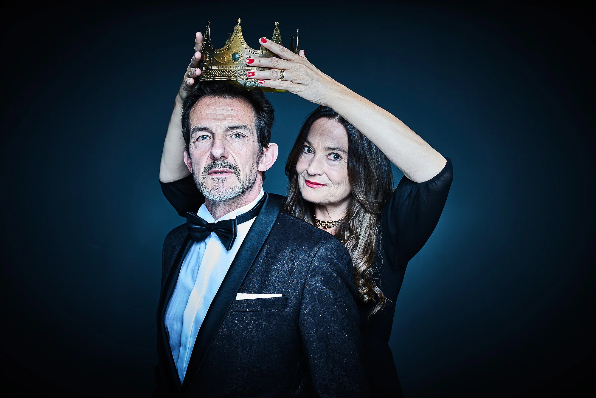 Einem Mann in Anzug wird von einer Frau eine Krone aufgesetzt.