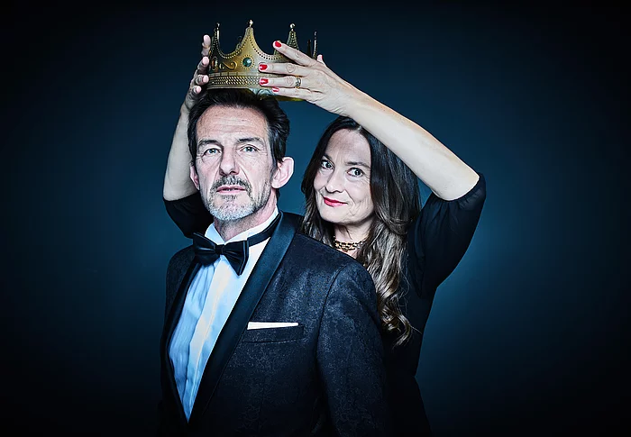 Einem Mann in Anzug wird von einer Frau eine Krone aufgesetzt.
