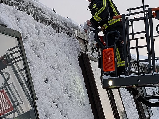 Ein Feuerwehrmann steht im Korb einer Drehleiter und entfernt Eisplatten vom Dach des Rathauses.