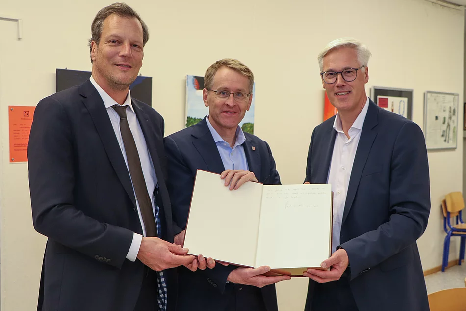Bürgervorsteher Claus Peters, Ministerpräsident Daniel Günther, Bürgermeister Rainhard Zug stehen nebeneinander und halten das Goldene Buch der Stadt Glinde