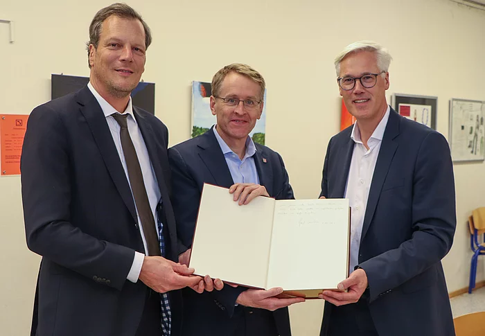 Bürgervorsteher Claus Peters, Ministerpräsident Daniel Günther, Bürgermeister Rainhard Zug stehen nebeneinander und halten das Goldene Buch der Stadt Glinde