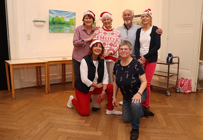 Sechs Personen haben sich zum Gruppenfoto versammelt. Sie tragen Weihnachtsmannmützen.