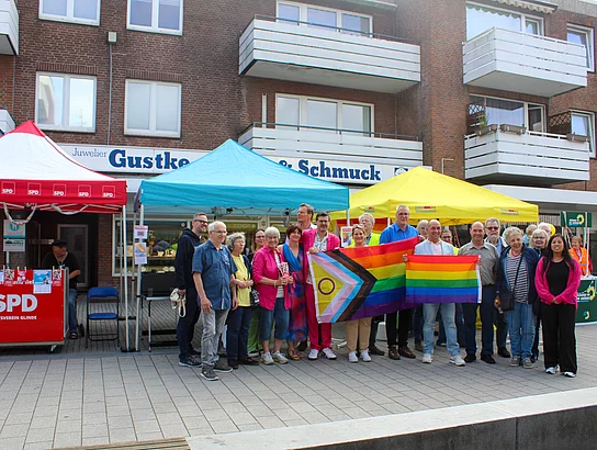 Eine Menschengruppe mit Regenbogenfahnen vor Parteiständen.