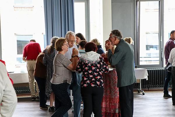 Menschen stehen einen Tisch, unterhalten sich und essen Häppchen.