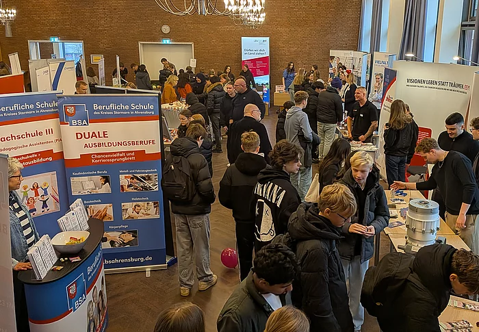 Viele junge Menschen stehen an Messeständen und unterhalten sich.