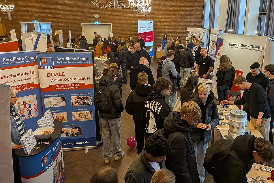 Viele junge Menschen stehen an Messeständen und unterhalten sich.