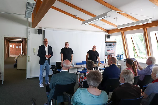 Drei Männer stehen vor Publikum und halten Reden.