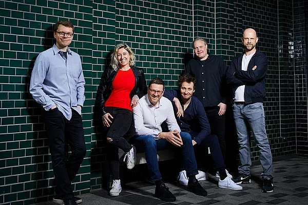Fünf Männer und eine Frau stehen zusammen an einer gefliesten Wand für ein Bandfoto.