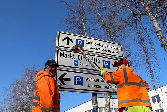 Zwei Menschen vom Baubetriebshof putzen ein großes Verkehrsschild.