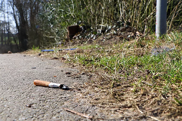 Ein Zigarettenstummel neben einen Mülleimer.