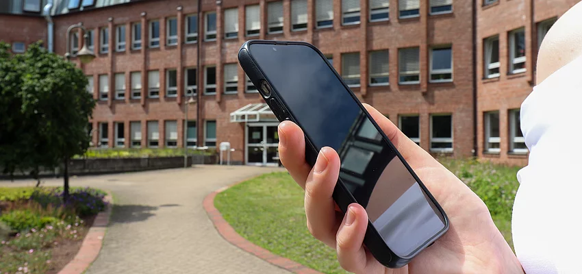 Symbolbild Smartphone in der Hand vor Rathaus Eine Hand hält ein Smartphone vor dem Glinder Rathaus