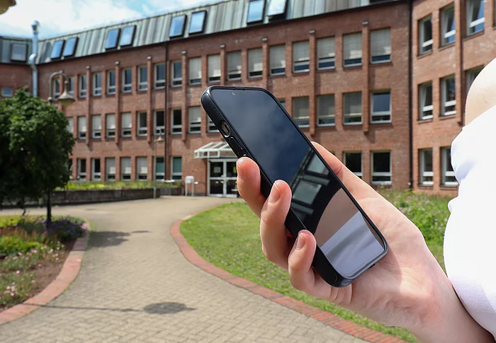Eine Hand hält ein Smartphone vor dem Glinder Rathaus