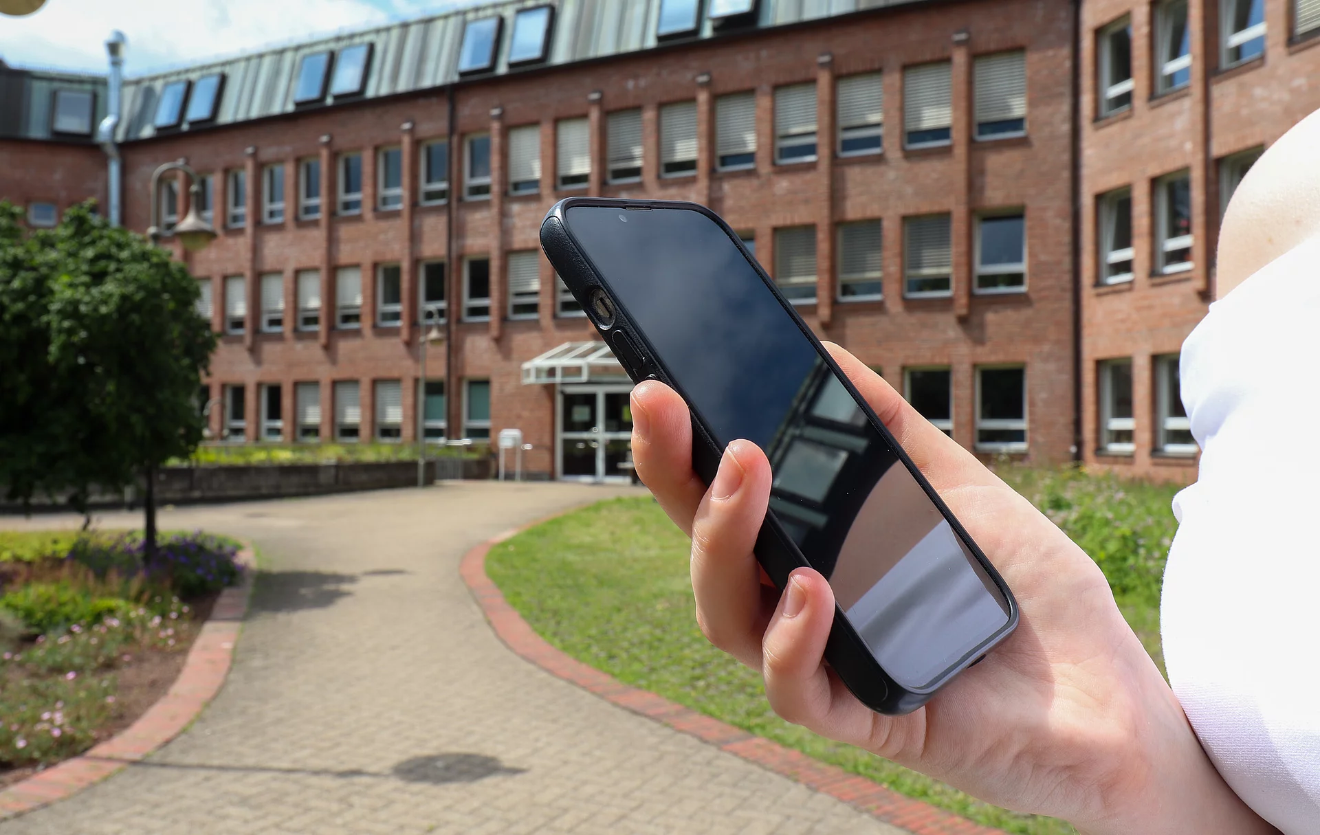 Eine Hand hält ein Smartphone vor dem Glinder Rathaus