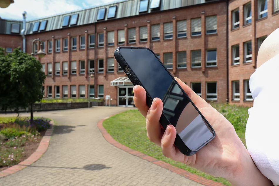 Symbolbild Smartphone in der Hand vor Rathaus Eine Hand hält ein Smartphone vor dem Glinder Rathaus