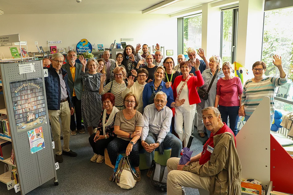 Eine Menschengruppe steht zwischen Bücherregalen und winkt.