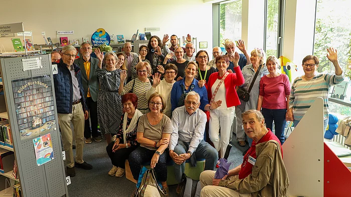 Eine Menschengruppe steht zwischen Bücherregalen und winkt.