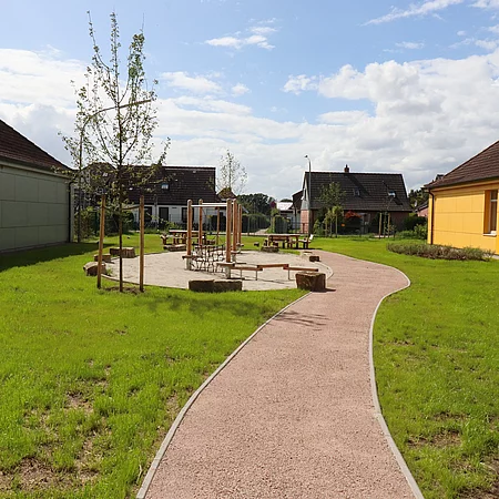 Zwischen zwei flachen Schulgebäuden sind Sitzbänke im Halbrund aufgestellt. Der Bereich ist für Unterricht im Freien vorgesehen.