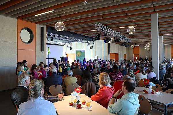 Eine Kindergruppe steht vor einer Bühne und singt